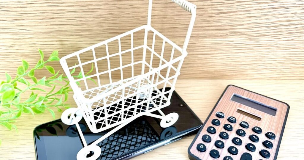 スマートフォンと電卓、ショッピングカートのミニチュアで表現されたネットショッピングの概念
