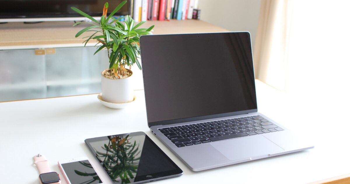 ノートパソコンとタブレットとスマートフォンが並ぶ白いデスク